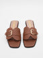 Sandalias marrón planas con hebilla dorada y puntera cuadrada.