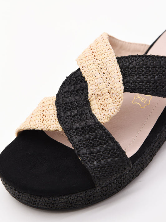 Sandalias planas de rafia con tiras cruzadas en negro y beige. Diseño cómodo, ligero y versátil.