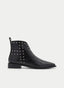 Botín plano de mujer en color negro, diseñado con silueta estilizada de punta fina, caña baja y detalle de tachuelas metálicas plateadas distribuidas en el lateral. Un modelo de estilo moderno con inspiración western y acabado sofisticado, ideal para looks de otoño-invierno, outfits urbanos y combinaciones casual chic con carácter.