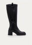 Bota alta de mujer en color negro con caña recta, puntera redondeada y tacón ancho. Presenta suela track dentada, cremallera lateral, tirador superior trasero y diseño liso de líneas elegantes con acabado sofisticado.