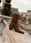 Botines cowboy de mujer AZAREY en tono camel con acabado tipo ante, tacón ancho y detalle de hebilla con tachuelas metálicas. Su diseño de inspiración western aporta personalidad y estilo a los looks de temporada, manteniendo una silueta femenina y fácil de combinar. Un botín versátil para llevar con vestidos, faldas o pantalones, ideal para crear conjuntos urbanos, casuales o sofisticados con un toque actual.