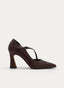 Zapato de salón femenino en color marrón, con punta fina, abertura lateral y tira cruzada sobre el empeine de un lado a otro. Presenta hebilla metálica ajustable y tacón alto ancho con base ligeramente acampanada.