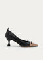 Zapato salón bicolor en negro y nude, con punta fina, escote bajo y detalles negros redondeados sobre la puntera. Presenta tacón medio tipo copa, silueta cerrada y tirador trasero.