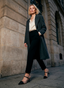 Zapatos de salón de mujer AZAREY en diseño bicolor negro y beige, con puntera fina, pulsera al empeine y tacón medio estilizado. La imagen muestra el calzado combinado con un look urbano elegante, con pantalón negro, camisa satinada y abrigo largo, resaltando su estilo sofisticado y versátil. Un zapato ideal para oficina, eventos, invitadas o looks de diario con un toque refinado, pensado para aportar comodidad, tendencia y elegancia atemporal.